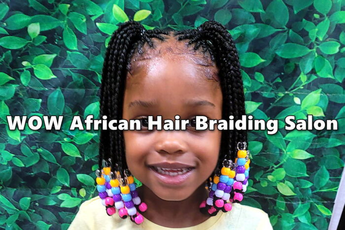 Child with stylish box braids with multicolored beads smiling at kids hair salon.